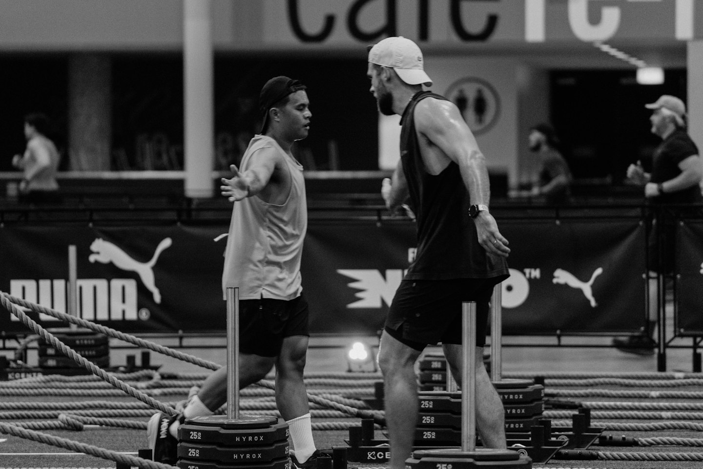 Twee mannen duwen verzwaarde sleeën over een binnenvloer in de sportschool.