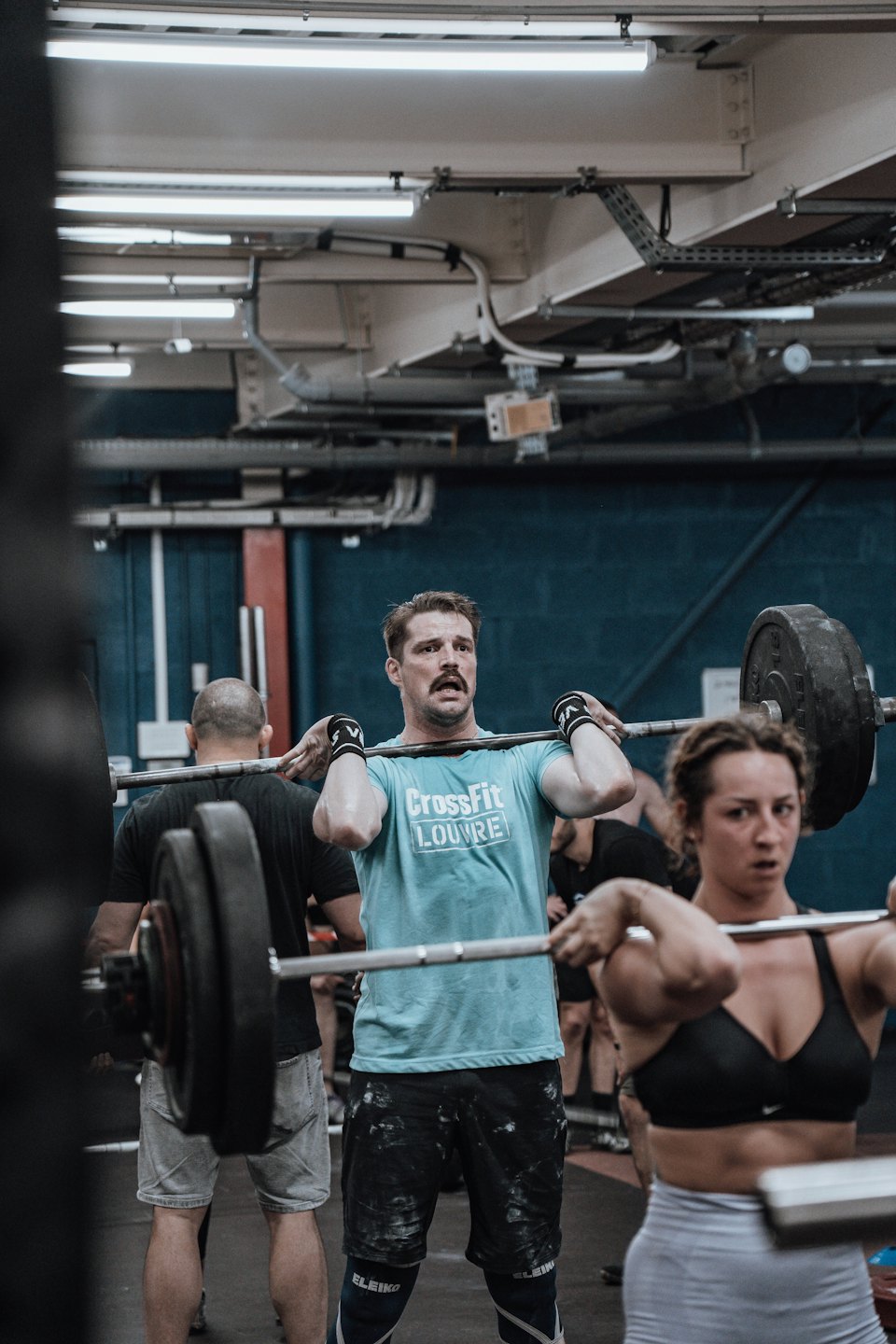 Atleten tillen barbells in een front-rack positie in een sportschool.